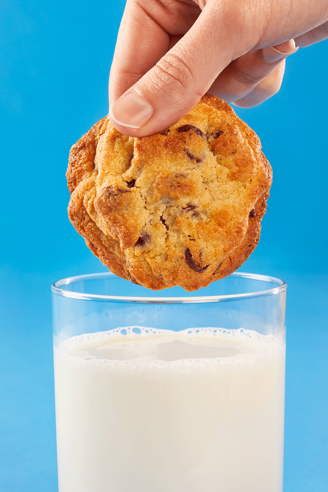 An animated gif featuring a close-up view of a hand holding a chocolate chip cookie and dunking it in a glass of milk.