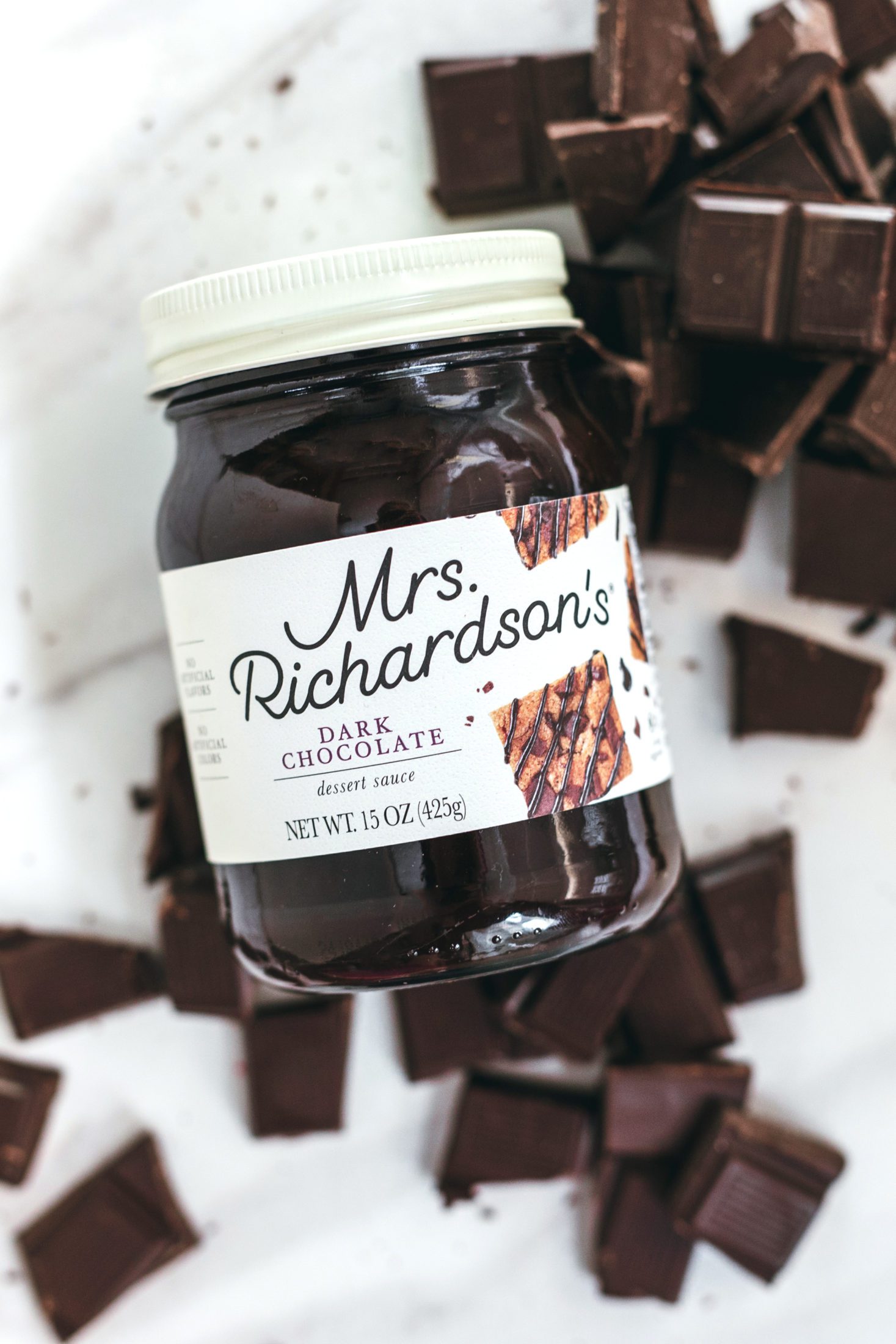 An overhead view of new Mrs. Richardson's cream label design using a clear glass jar with cream white lid. Dark Chocolate dessert sauce jar with chopped chocolate pieces on a marble surface.