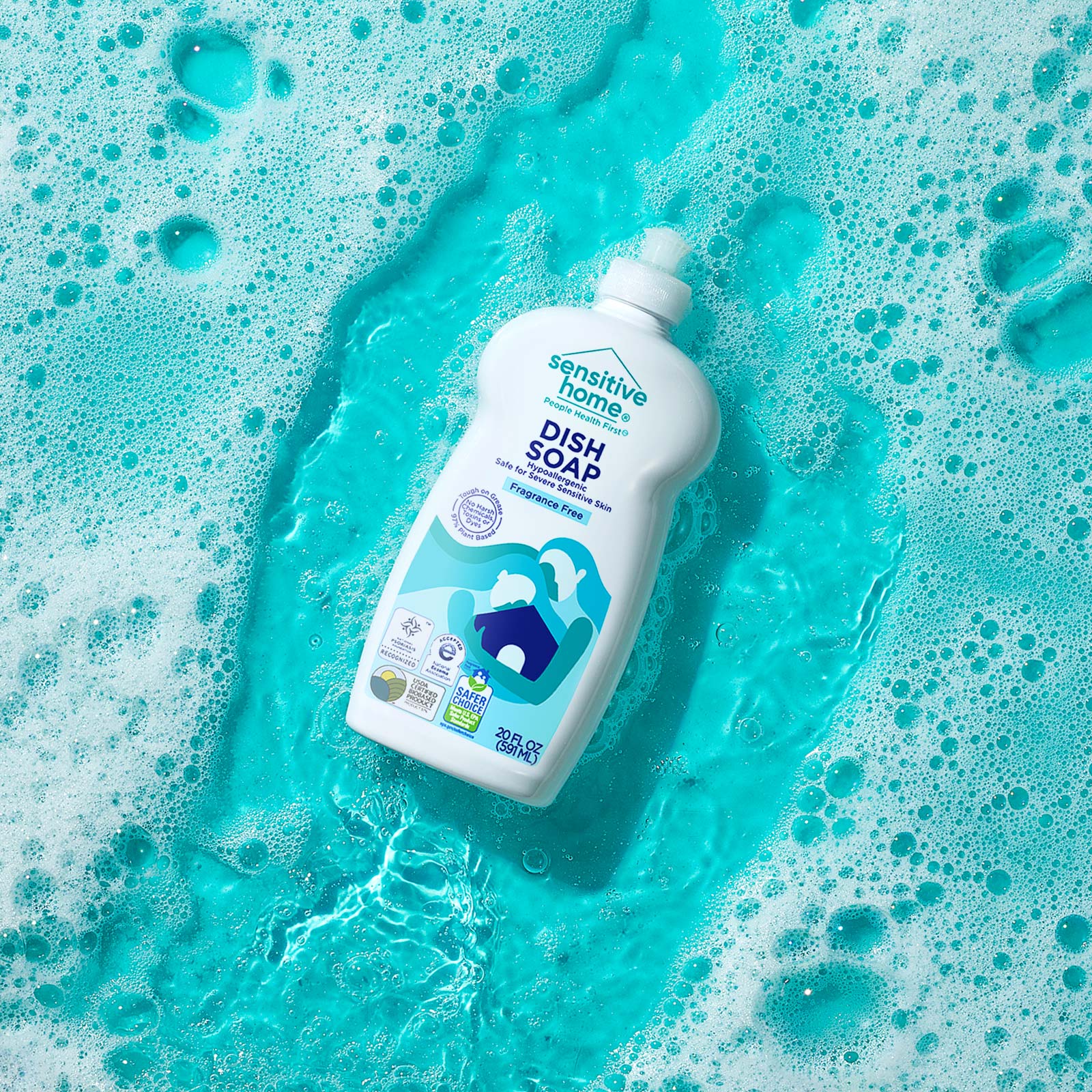 A bottle of Sensitive Home Laundry Detergent - Free & Clear floating in soapy water over a light blue surface.