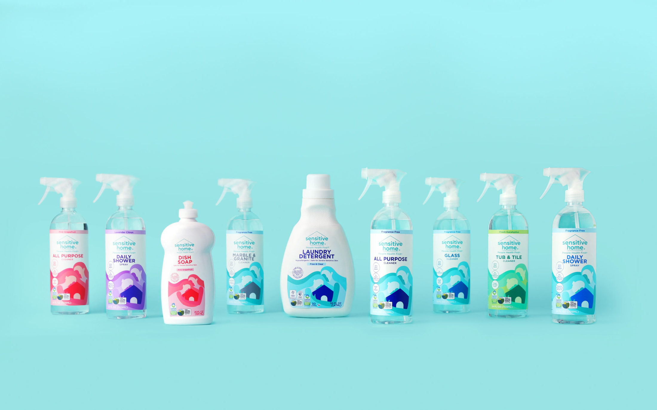 A lineup of Sensitive Home products featuring spray bottle cleaners, dish soap, and laundry detergent photographed on a light blue background.