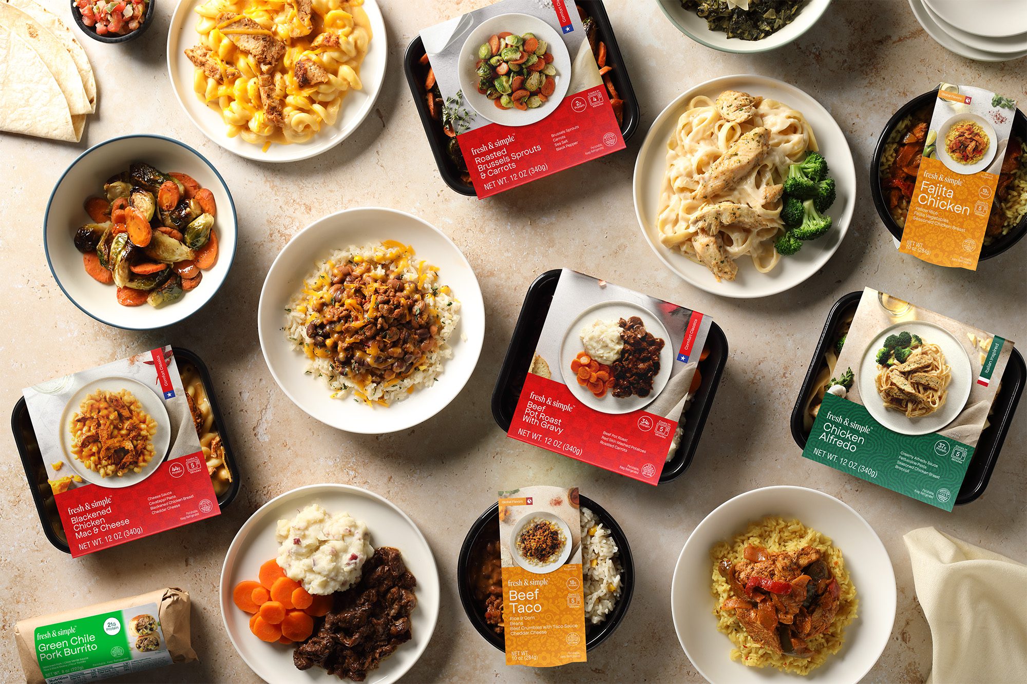 A range of Fresh & Simple products both in and out of packaging. Dishes include Blackened Chicken Mac & Cheese, Green Chile Pork Burrito, Roasted Brussel Sprouts & Carrots, Beef Pot Roast with Gravy, Beef Taco Bowl, Fajita Chicken Bowl, and Chicken Alfredo.
