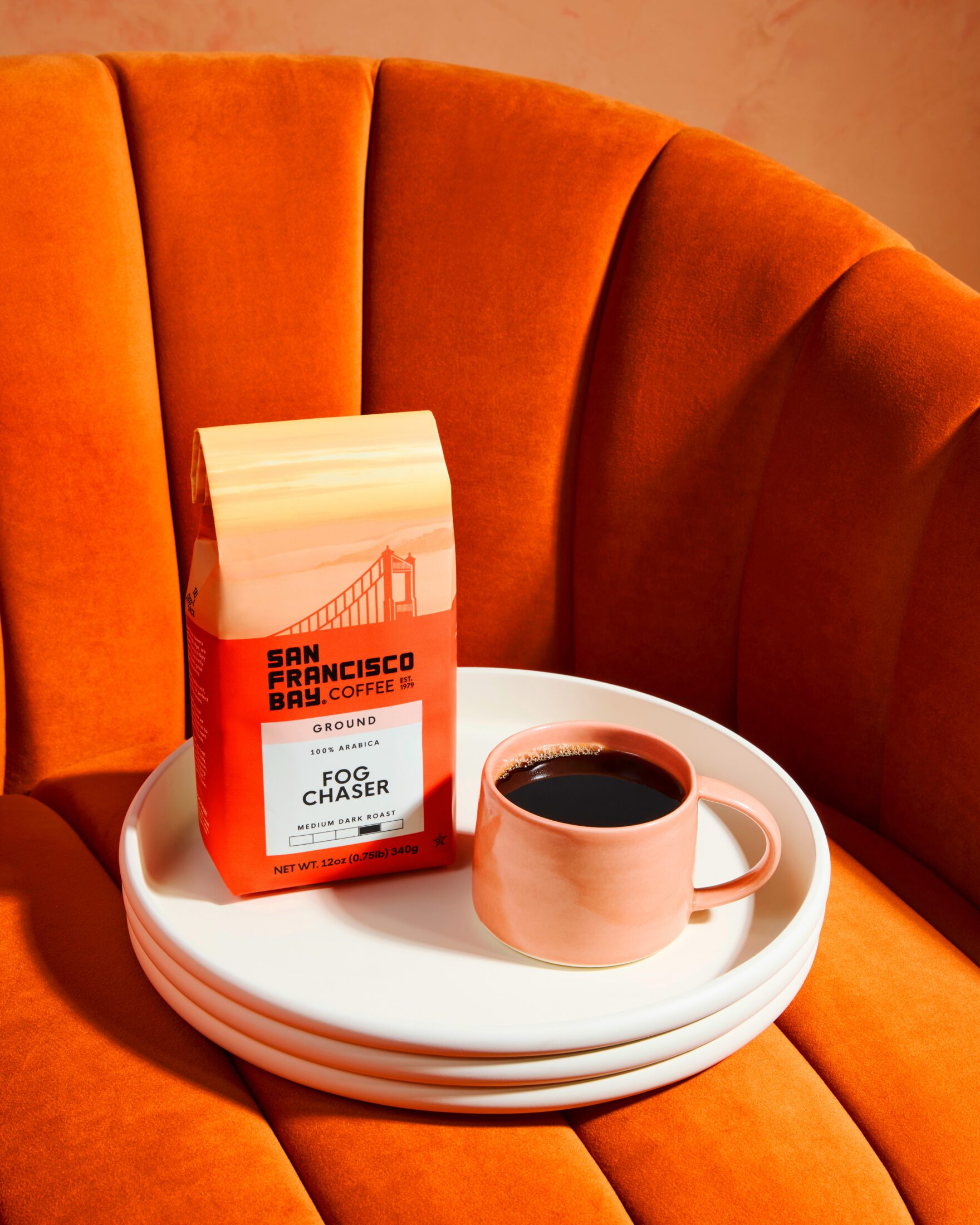 A bag of San Francisco Bay Coffee Fog Chaser Ground 12 oz on a orange chair with a fresh cup of coffee
